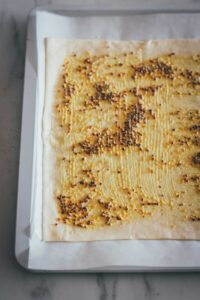 Der auf dem Blech dünn ausgerollte Blätterteig wird mit zwei Sorten Senf bestrichen.