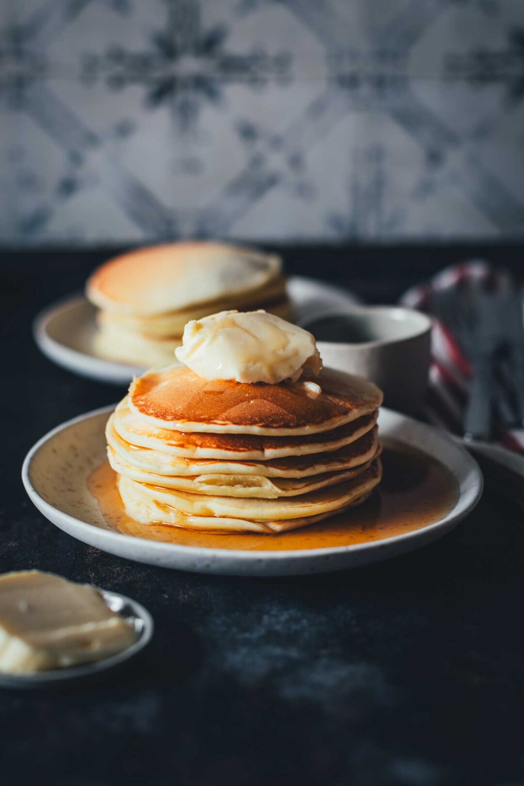 Pancakes – mein absolutes Lieblingsrezept seit über 15 Jahren. Einfach ein Stapel Pancakes mit Butter und Ahornsirup serviert auf einem kleinen Teller | moeyskitchen.com