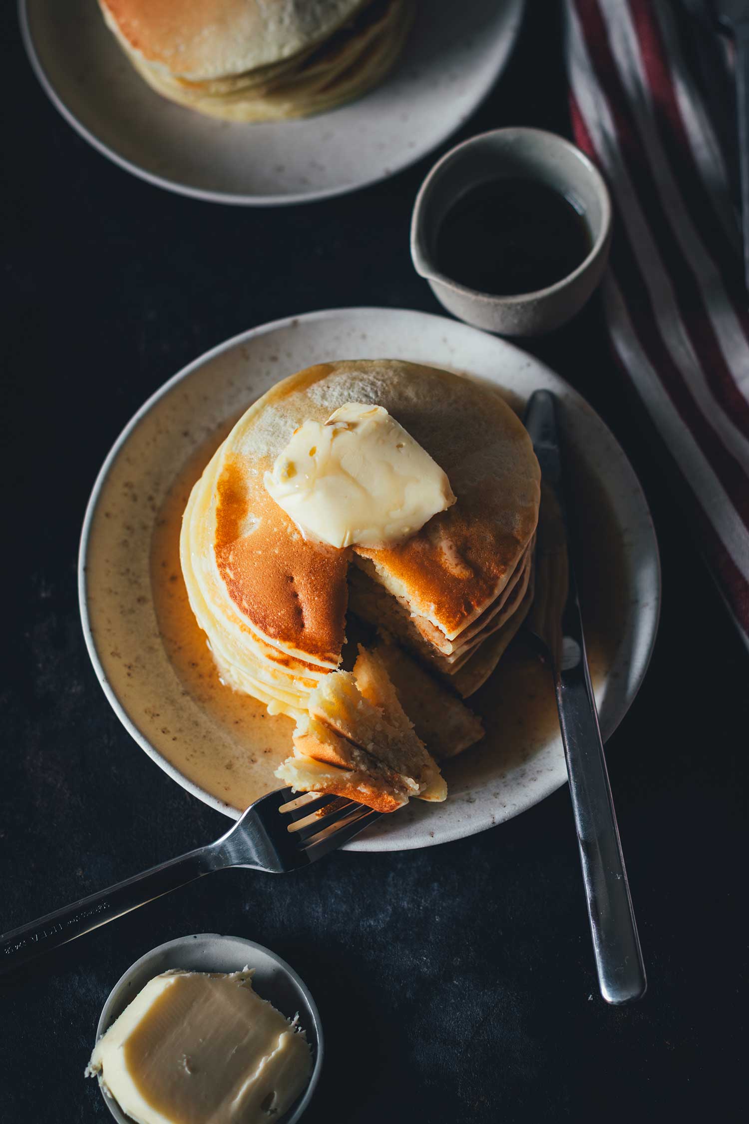Ein Stapel Pancakes von oben fotografiert und mit Messer ud Gabel angeschnitten. Serviert mit Butter und Ahornsirup | moeyskitchen.com