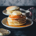 Ein Stapel Pancakes, seitlich fotografiert als quadratisches Bikd. 6 Pancakes auf einem kleinen Teller, übereinander gestapelt und mit einem Stück Salzbutter und Ahornsirup serviert | moeyskitchen.com