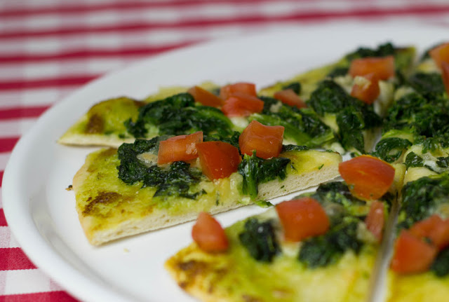 frisch angeschnittene Pizza mit Pesto, Spinat, Knoblauchöl und Tomatenwürfeln