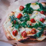 Seitliche Ansicht auf einen frisch gebackenen, knusprigen Flammkuchen mit Spargel. Zusätzlich belegt mit kleinen Tomaten, Rucola und Ziegenkäserolle perfekt für den Frühling!