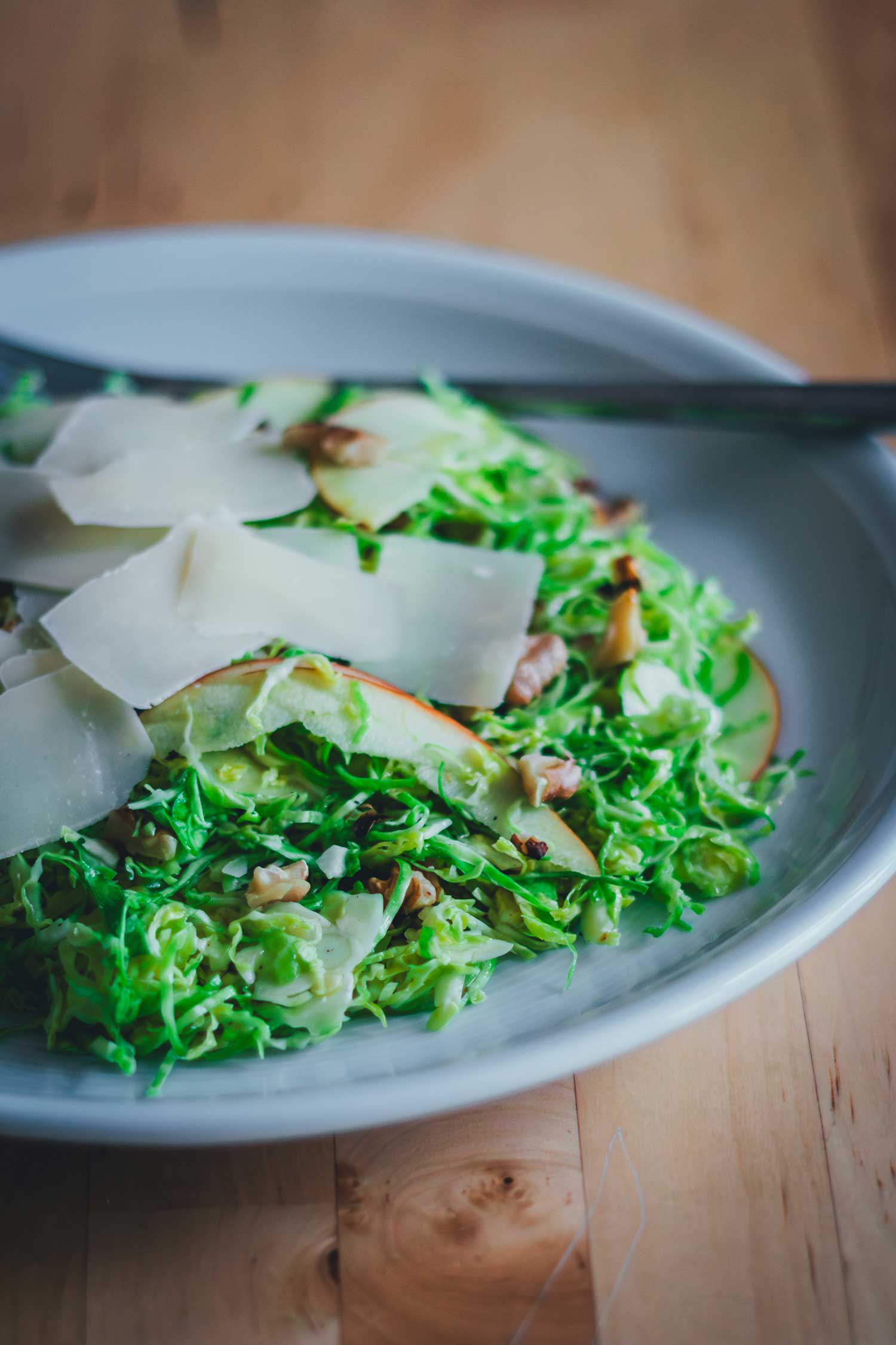 Fein gehobelter Rosenkohlsalat mit Apfelscheiben, Walnüssen und Pecorino auf einem Teller