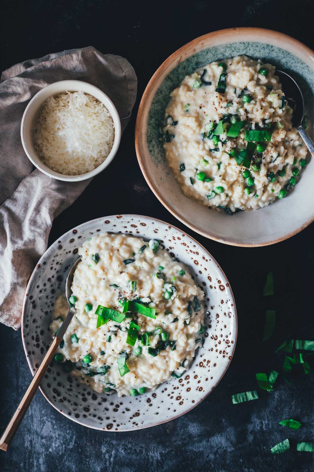 Topshot Ansicht von zwei tiefen Tellern mit Bärlauch-Risotto. Man sieht das cremige Risotto auf den Tellern, getoppt mit frischem Bärlauch und serviert mit geriebenem Käse.