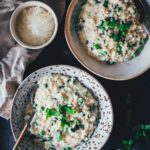 Topshot Ansicht von zwei tiefen Tellern mit Bärlauch-Risotto. Man sieht das cremige Risotto auf den Tellern, getoppt mit frischem Bärlauch und serviert mit geriebenem Käse.