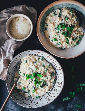 Topshot Ansicht von zwei tiefen Tellern mit Bärlauch-Risotto. Man sieht das cremige Risotto auf den Tellern, getoppt mit frischem Bärlauch und serviert mit geriebenem Käse.