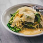 Pasta mit grünem Spargel und Parmesansauce auf einem Teller mit Parmesanspänen serviert, seitlich zu sehen.
