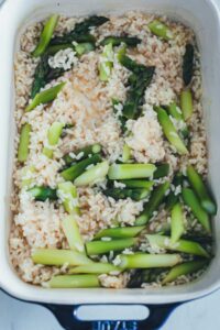 Arborio-Reis und grüner Spargel in heißer Brühe in einer Staub-Auflaufform vor dem Garen im Ofen