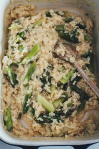 Cremiges Ofenrisotto mit grünem Spargel nach dem Garen, mit Holzlöffel in der Auflaufform angerichtet