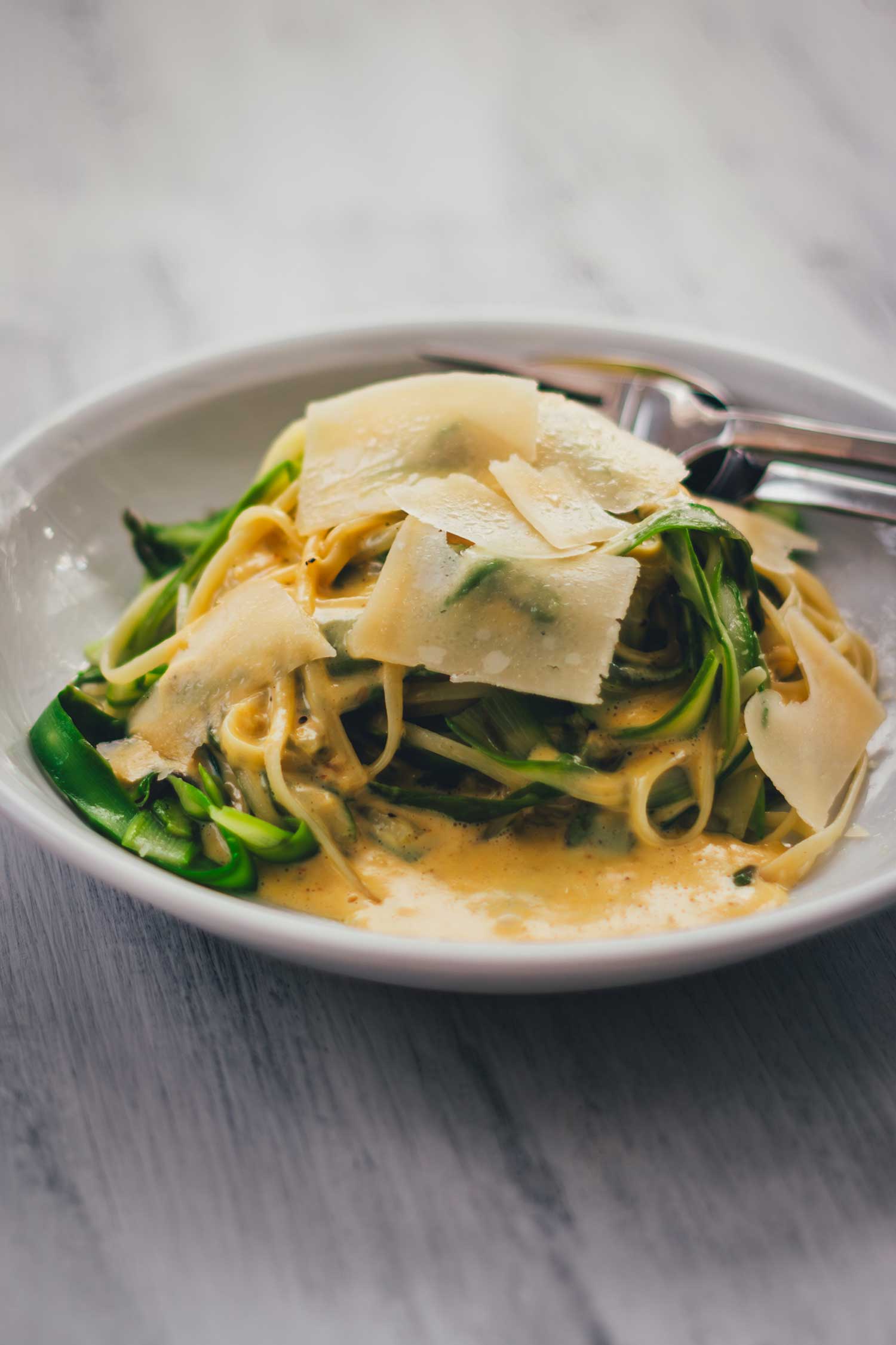 Cremige Parmesansauce und Pasta mit grünem Spargel servierbereit und mit Parmesan bestreut auf einem weißen Teller.