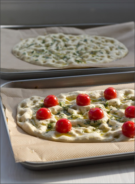 frisch gebackenes Focaccia mit Rosmarin und Meersalz und Tomaten und Kräutern Teig für Focaccia mit Rosmarin und Meersalz und Tomaten mit Kräutern, vor dem Backen auf dem Backblech