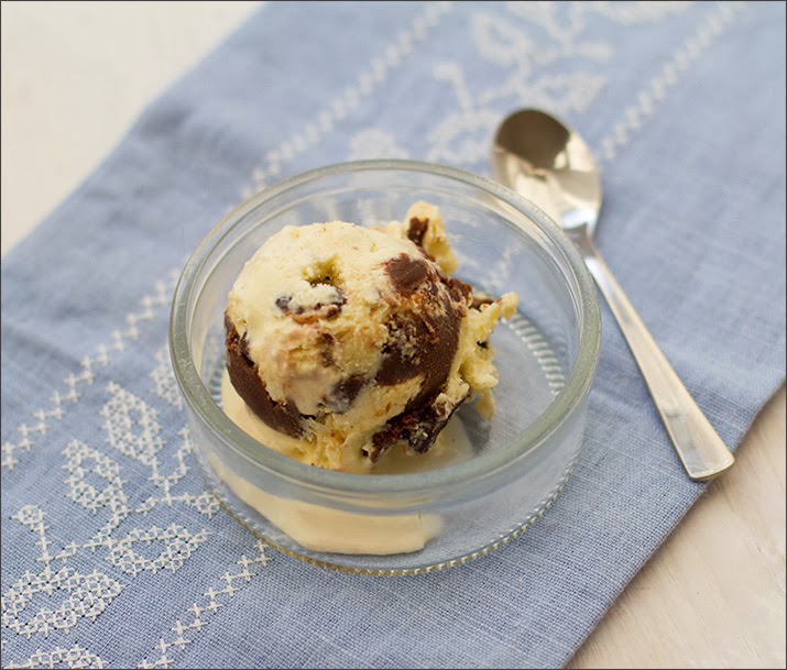 Eine Kugel Vanilleeis mit Schoko-Erdnüssen und Schoko-Fudge, serviert in einem Gläschen.