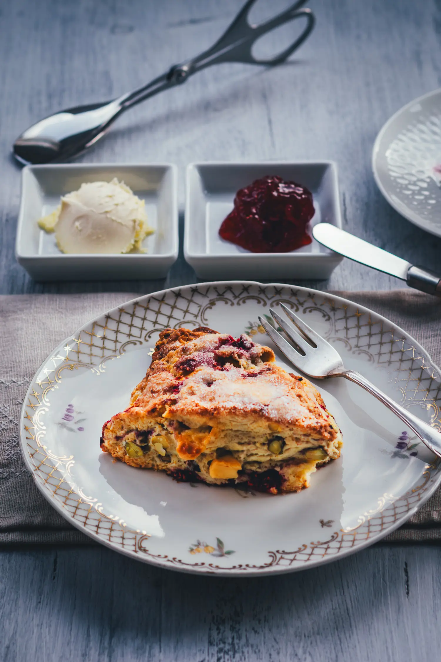 Ein Himbeer Scone auf einem Vintage-Teller, im Hintergrund Clotted Cream und Himbeerkonfitüre in weißen Schälchen