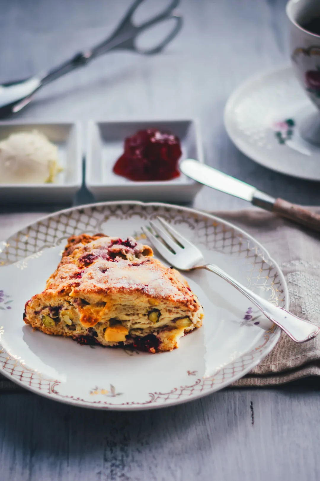 Himbeer Scones mit Pistazien und weißer Schokolade auf einem Goldrand-Teller, dazu Clotted Cream und Himbeerkonfitüre in kleinen Schälchen