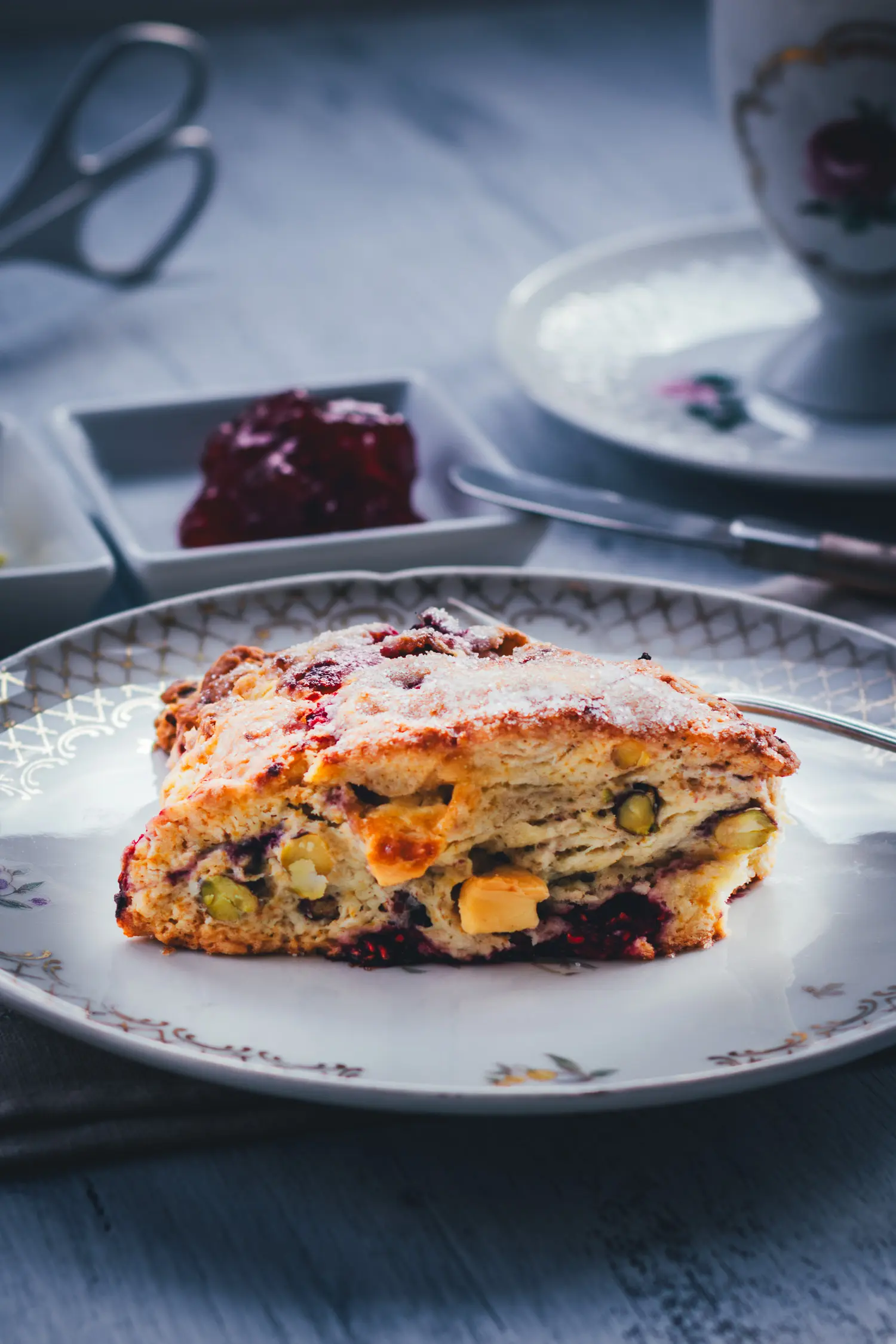 Nahaufnahme eines Himbeer Scones mit sichtbaren Pistazien, Stücken weißer Schokolade und Himbeeren im buttrigen Teig