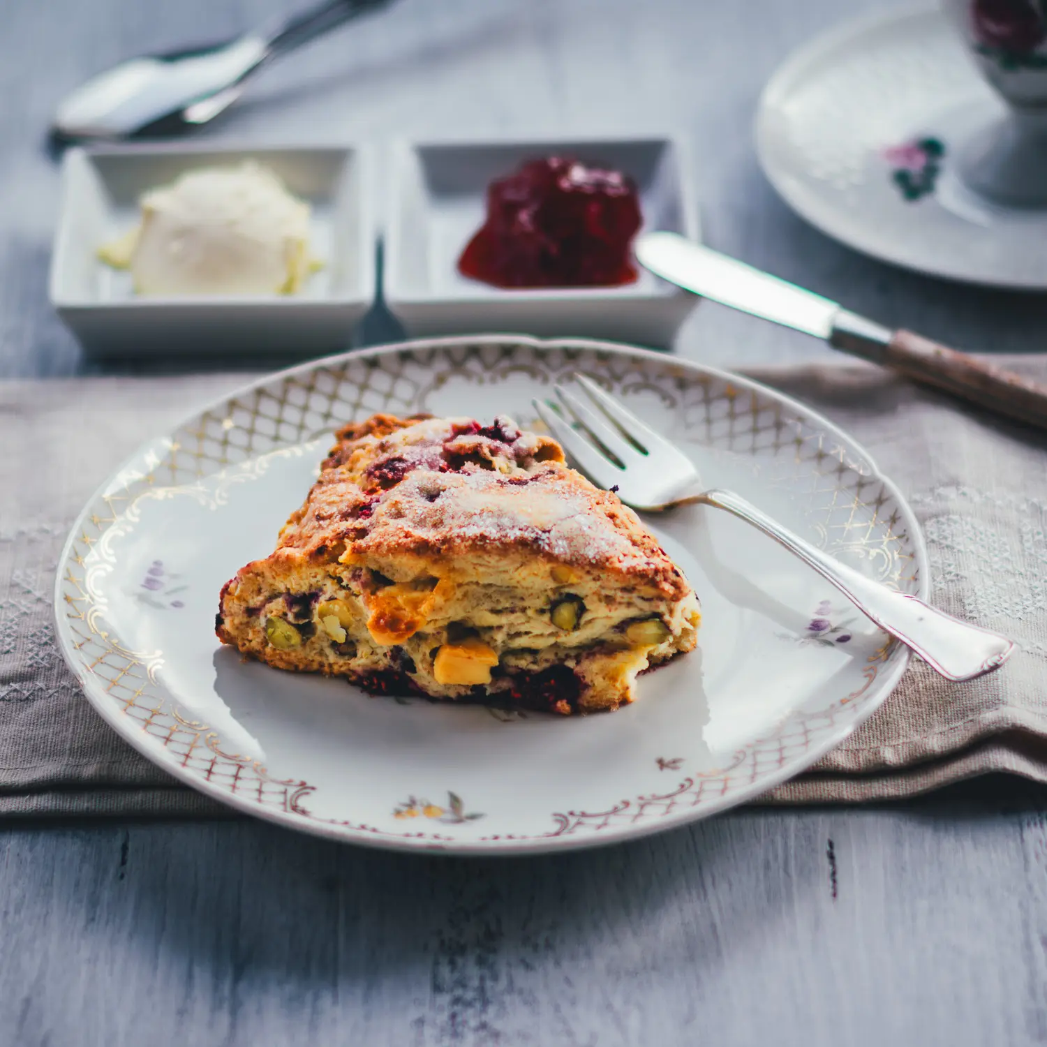 Himbeer Scones mit Pistazien und weißer Schokolade, frisch gebacken und mit Zucker bestreut, serviert mit Clotted Cream und Konfitüre