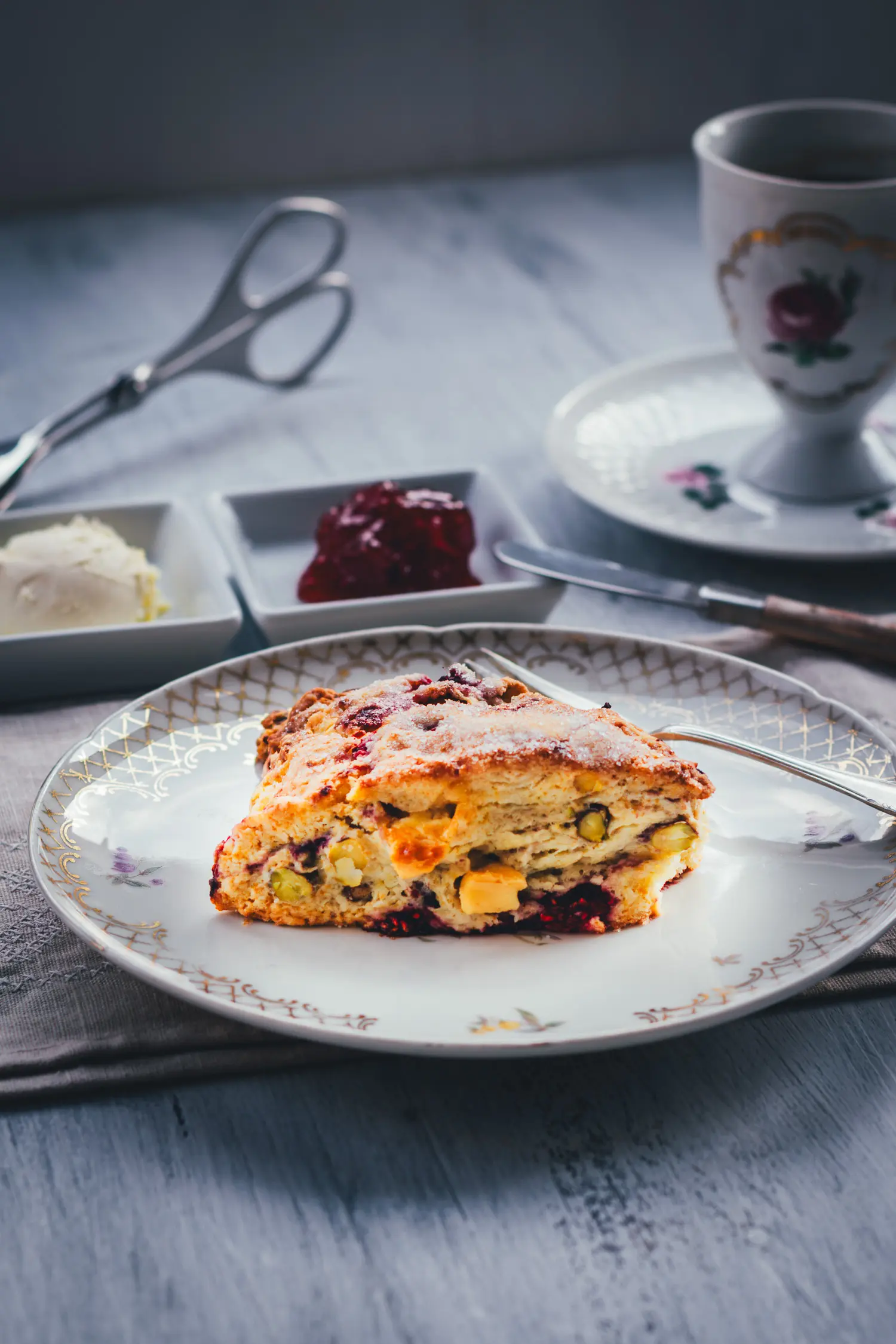 Himbeer Scones zur Tea Time mit Teetasse, Clotted Cream und Konfitüre auf einem grauen Holztisch