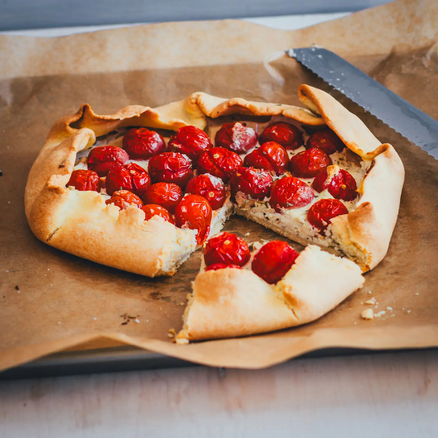 Tomaten-Galette mit Ricotta und ganzen Kirschtomaten, aufgeschnitten auf einem mit Backpapier ausgelegten Blech