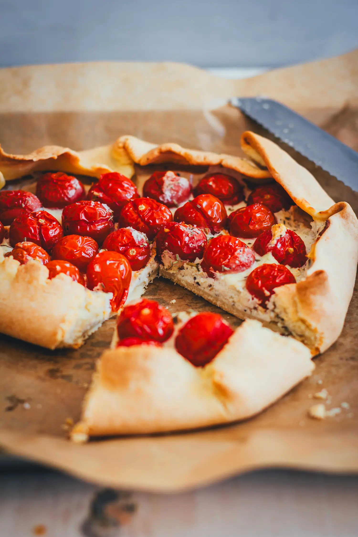 Herausgelöstes Stück Tomaten-Galette vor der angeschnittenen Galette auf Backpapier