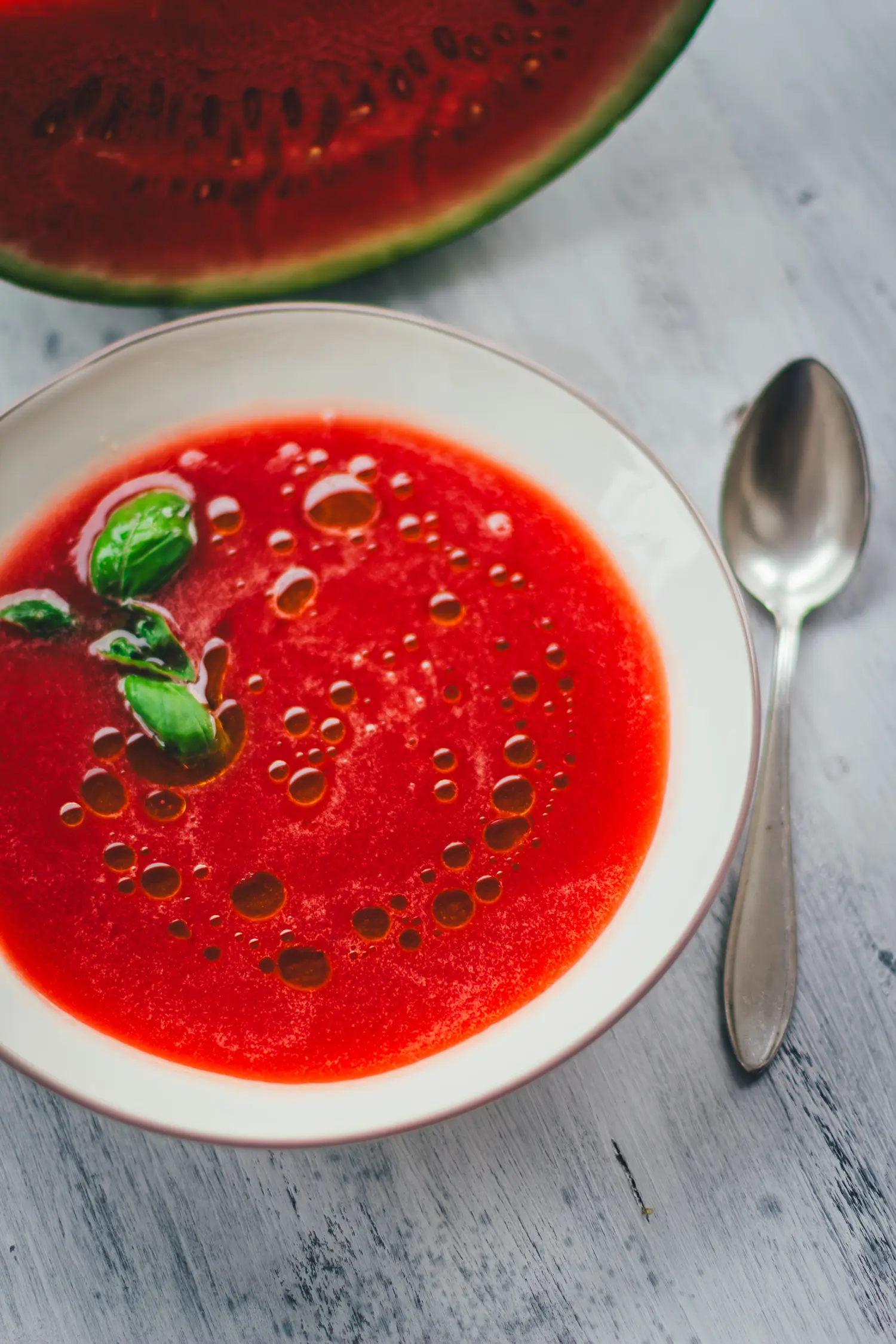 Seidig pürierte Wassermelonen-Gazpacho mit Olivenöl und Basilikum in einer weißen Schale