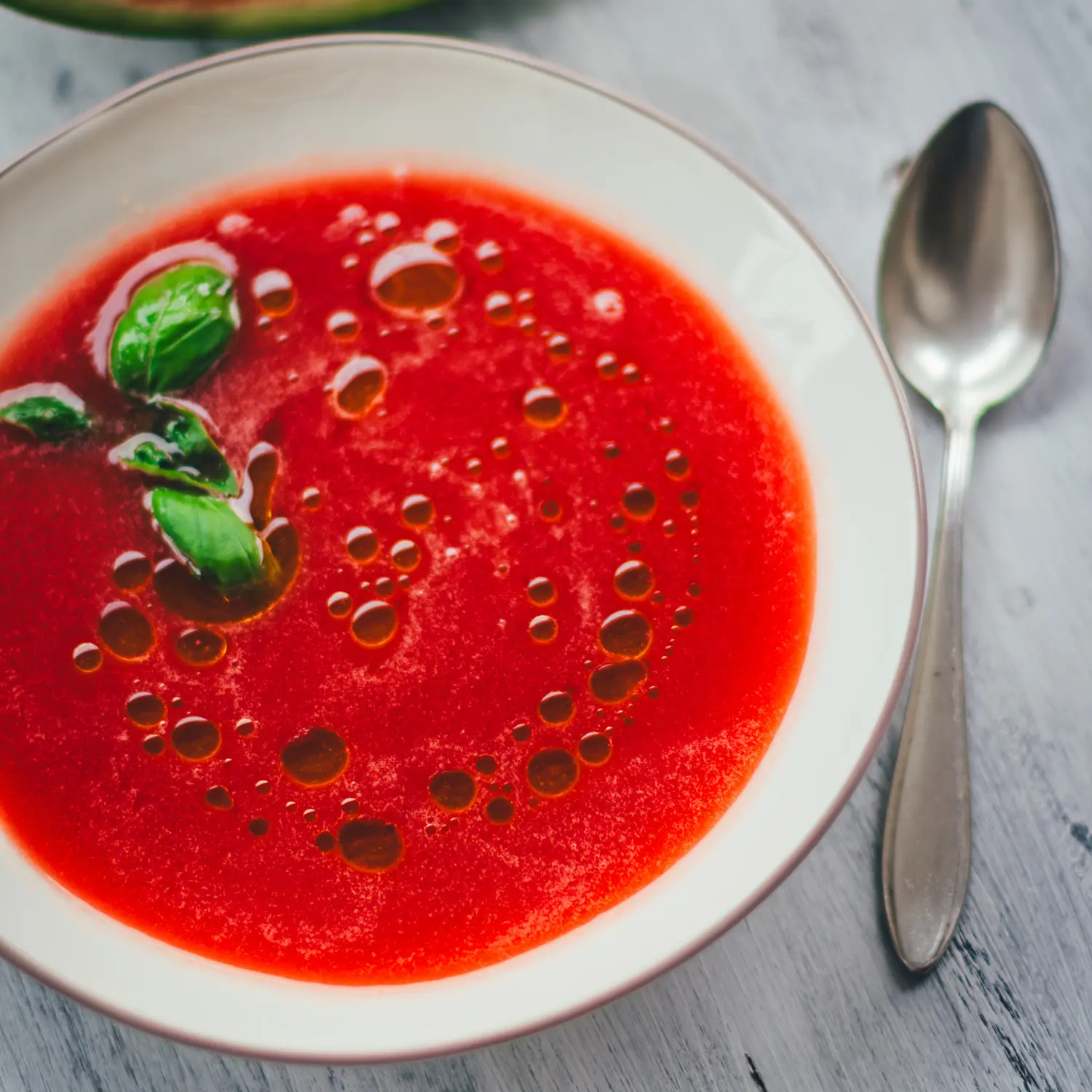 Cremige Wassermelonen-Gazpacho mit Olivenöl-Tropfen und Basilikum, von oben fotografiert
