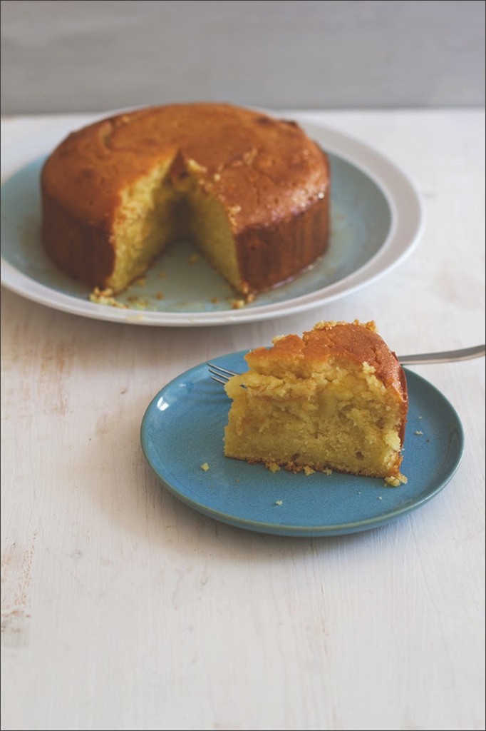 Rezept für Semolina-Joghurt-Kuchen mit Zitronensirup Ein Stück Semolina-Joghurt-Kuchen mit Zitronensirup auf dem Teller, im Hintergrund der angeschnittene Kuchen