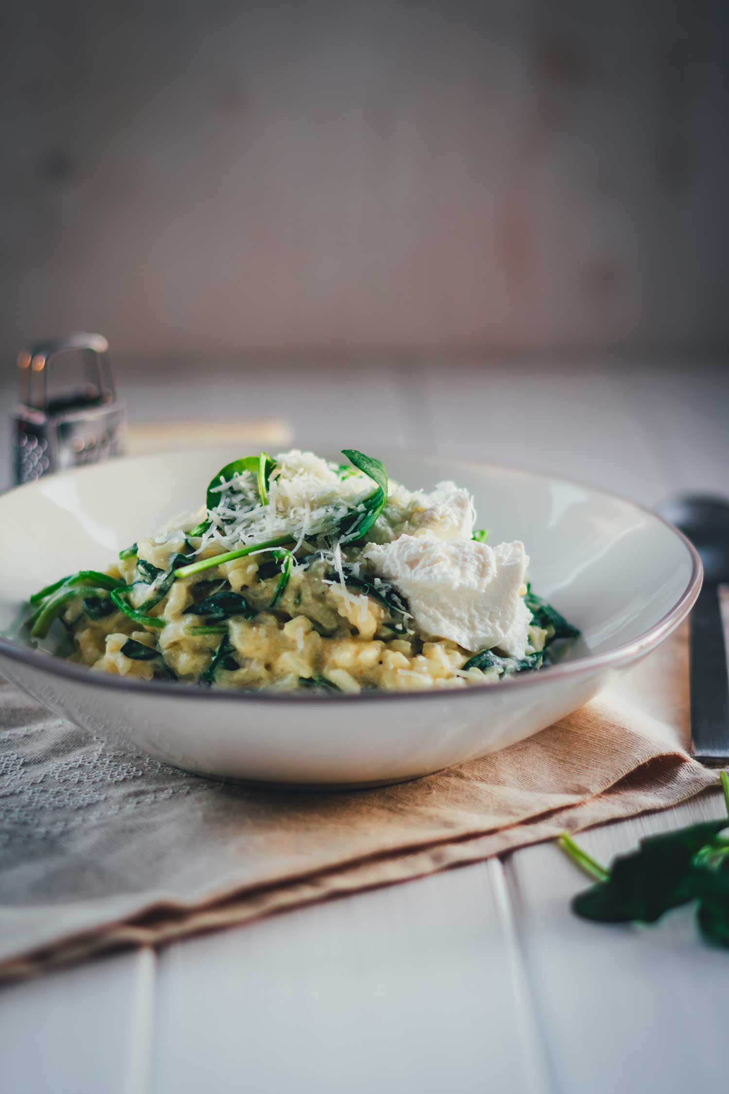 Frontale Ansicht in Nahaufnahme einer Schale mit Ofenrisotto mit Spinat, getoppt mit Ricotta und geriebenem Parmesan sowie frischem Babybspinat.