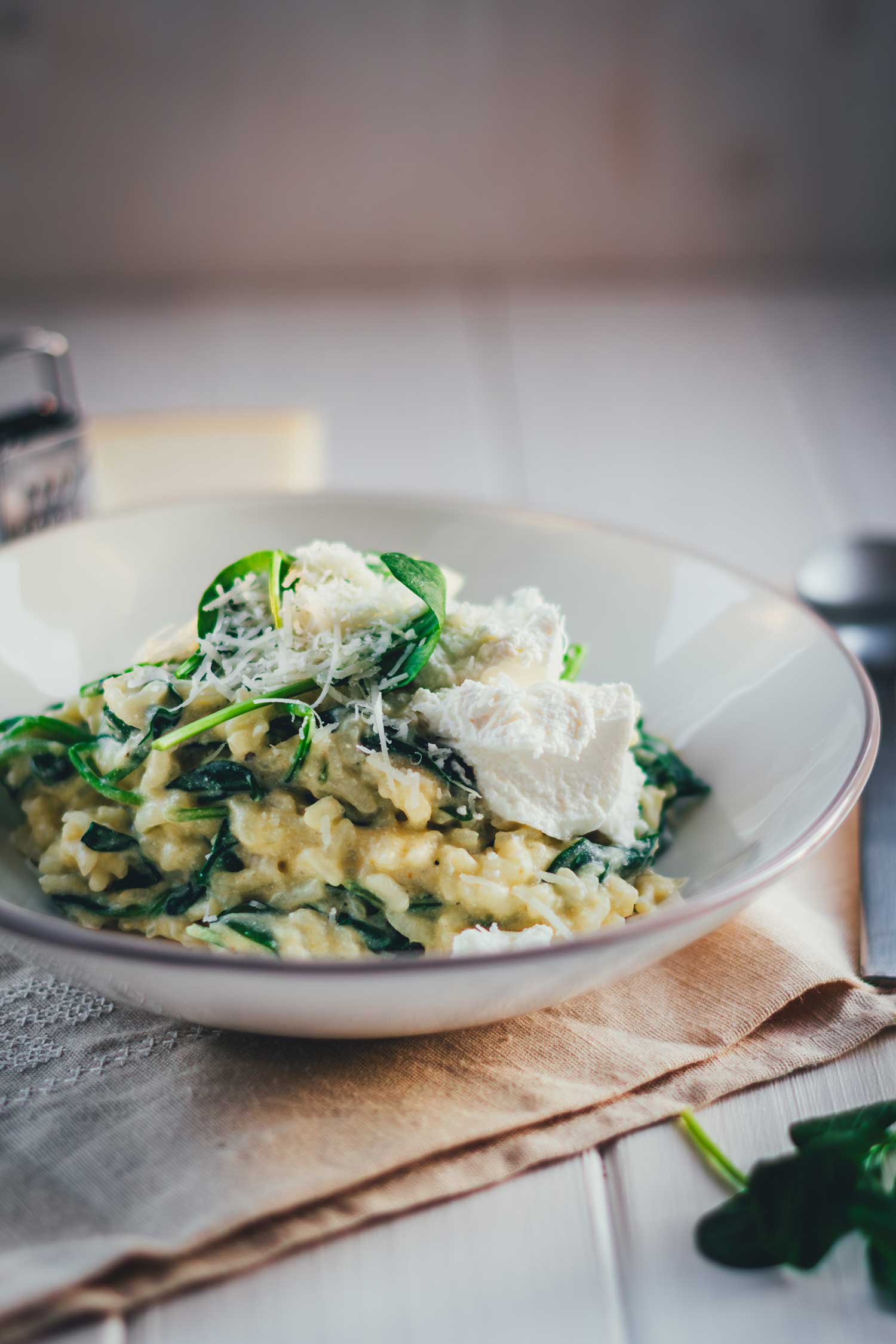 Leicht schräge Draufsicht auf Ofenrisotto mit Spinat, serviert in einer tiefen hellgrauen Schale. Bestreut mit Parmesan und Spinat sieht man das cremige Risotto ganz ohne Rühren.