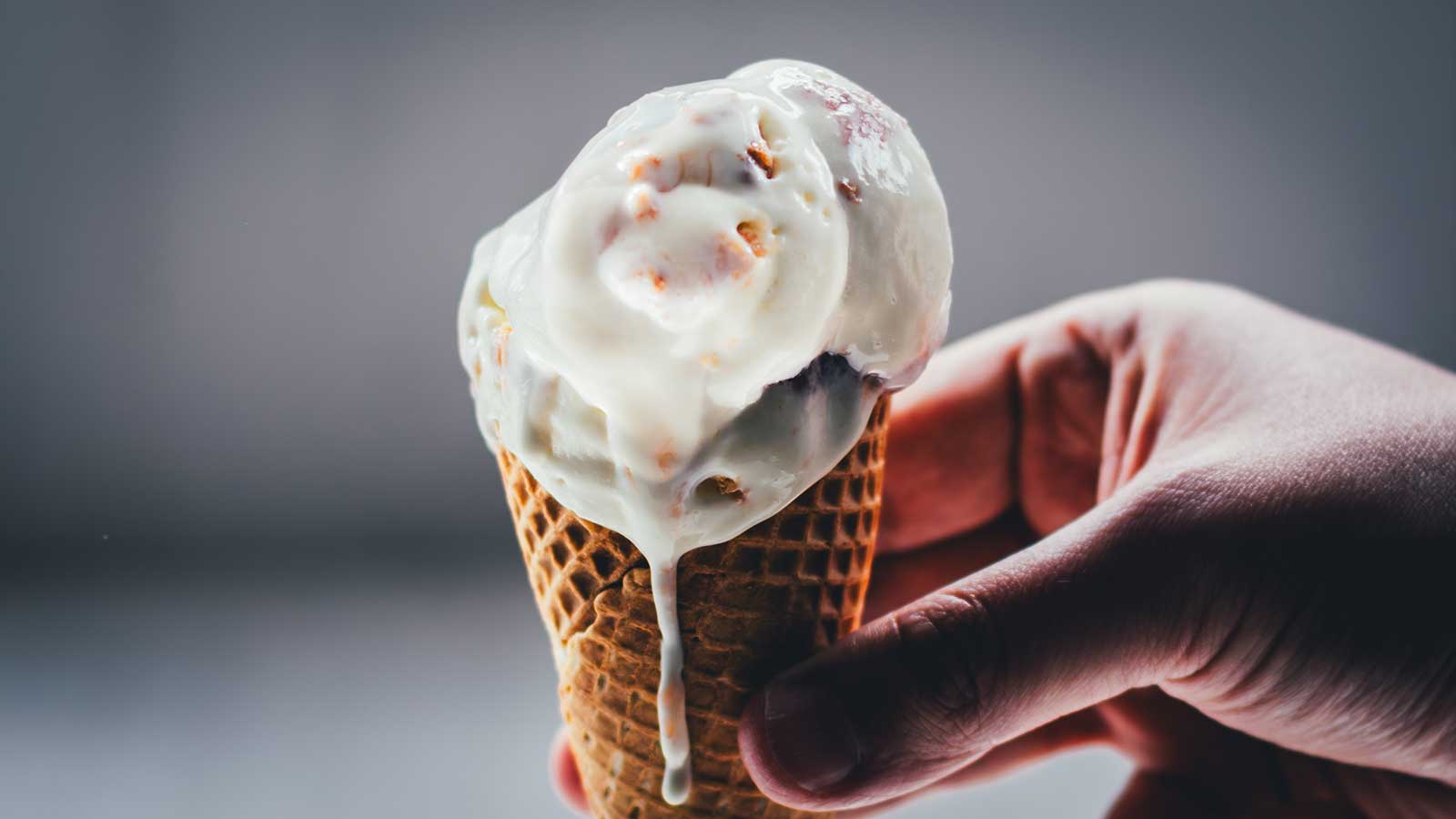 Rhabarber-Eis mit Streuseln auf einem Waffelkegel, von Hand gehalten
