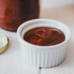 Selbstgemachter Rhabarberketchup in Glasflasche mit Schälchen voller Grillsauce und frischem Baguette