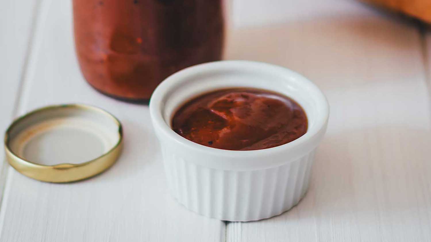 Selbstgemachter Rhabarberketchup in Glasflasche mit Schälchen voller Grillsauce und frischem Baguette