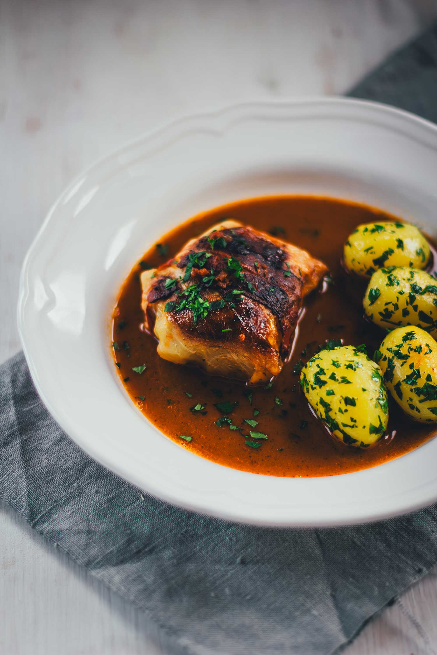 Klassische Kohlroulade auf Teller mit Petersilienkartoffeln und Sauce
