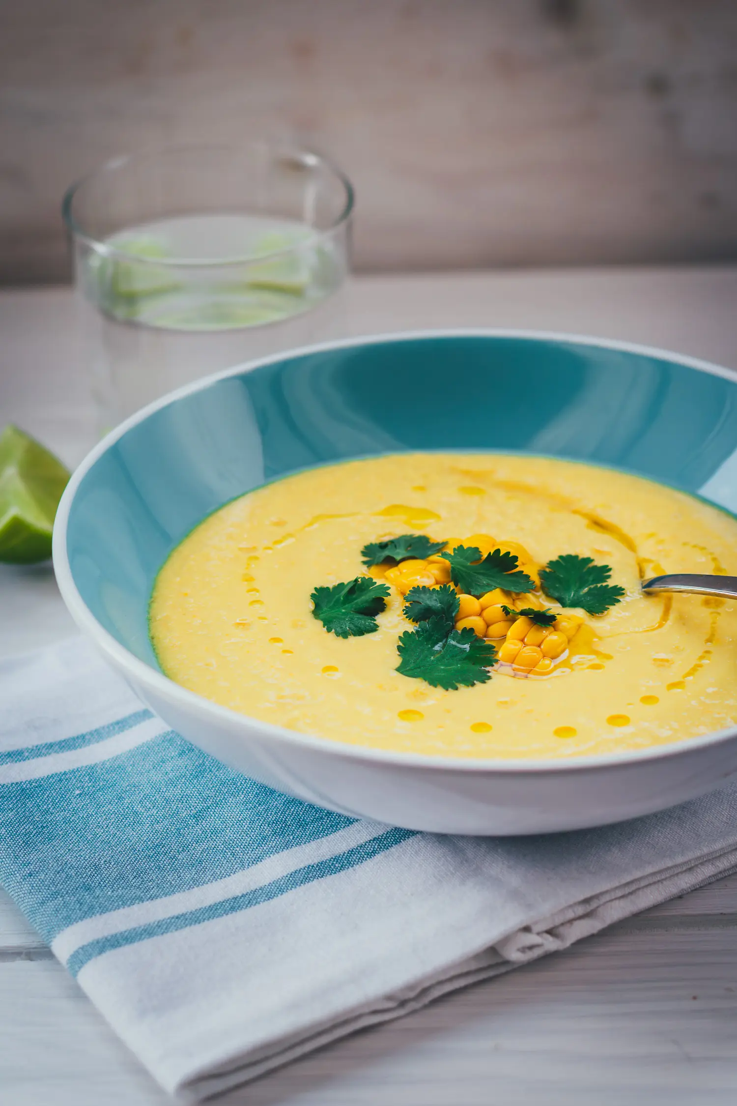 Seitliche Ansicht von einer Schale mit Mais-Paprika-Gazpacho, die mit Maiskörnern und Koriander getoppt wird.