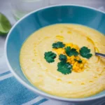 Nahaufnahme einer Schüssel, gefüllt mit kalter Mais-Paprika-Gazpacho, getoppt mit Maiskörnern und Koriander.
