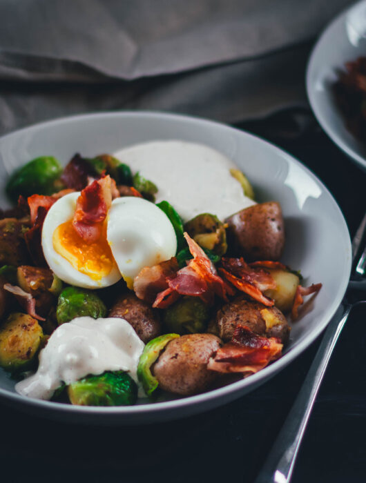 Hier teile ich mein Rezept für eine deftige Rosenkohl-Kartoffel-Pfanne. Serviert mit wachsweichem Ei, knusprigem Bacon und würzigem Knoblauch-Schmand. Perfekt für die schnelle Feierabendküche in Herbst und Winter! | moeyskitchen.com