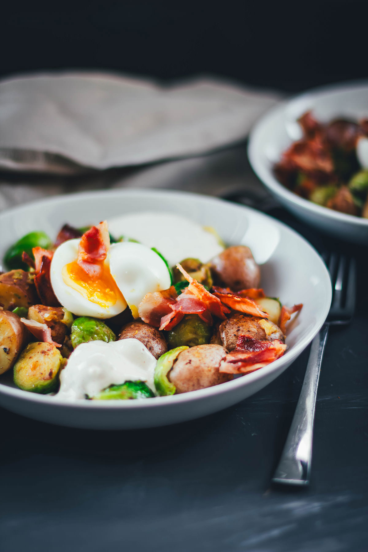 Hier teile ich mein Rezept für eine deftige Rosenkohl-Kartoffel-Pfanne. Serviert mit wachsweichem Ei, knusprigem Bacon und würzigem Knoblauch-Schmand. Perfekt für die schnelle Feierabendküche in Herbst und Winter! | moeyskitchen.com