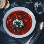 Topshot eines Tellers mit einer Portion Borschtsch (Borscht). Getoppt mit Saurer Sahne und Dill und mit etwas Brot serviert. | moeyskitchen.com