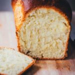 Nahaufnahme von einem frisch gebackenen und angeschnittenen Brioche-Brot auf einem Holzbrett. Man sieht die wattigweiche Krume und goldene Kruste. Daneben liegt ein Brotmesser.