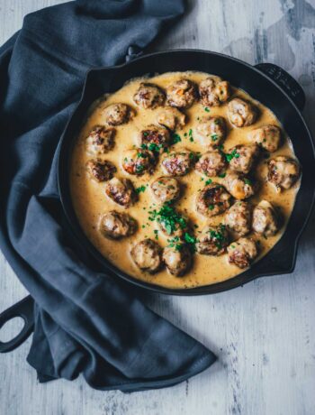 Köttbullar, schwedische Hackbällchen wie von IKEA werden in leckerer cremiger Sauce in einer gusseisernen Pfanne serviert. Die saftigen Hackbällchen sind mit Petersilie bestreut. Neben der Pfanne liegt ein Küchentuch. | moeyskitchen.com