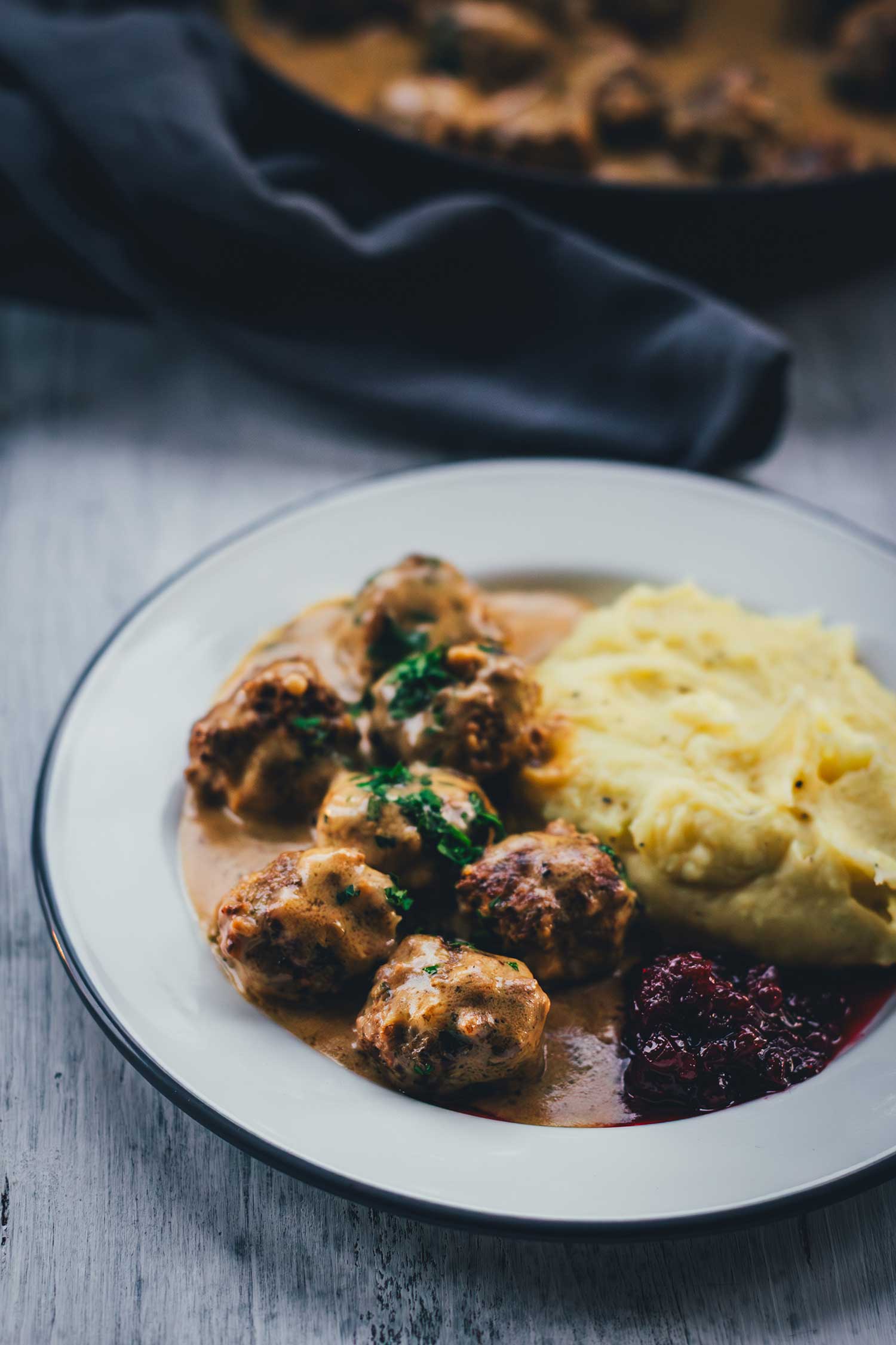 Ein Teller mit Köttbullar, schwedischen Hackfleischbällchen wird hier mit viel Sauce, selbst gemachtem Kartoffelpüree, Preiselbeeren und Petersilie serviert. | moeyskitchen.com