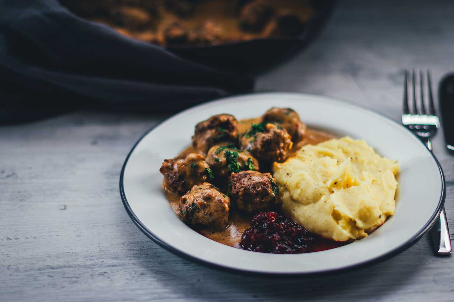 Seitliche Nahaufnahme eines Tellers mit Köttbullar in Sauce, Kartoffelpüree und Wildpreiselbeeren | moeyskitchen.com