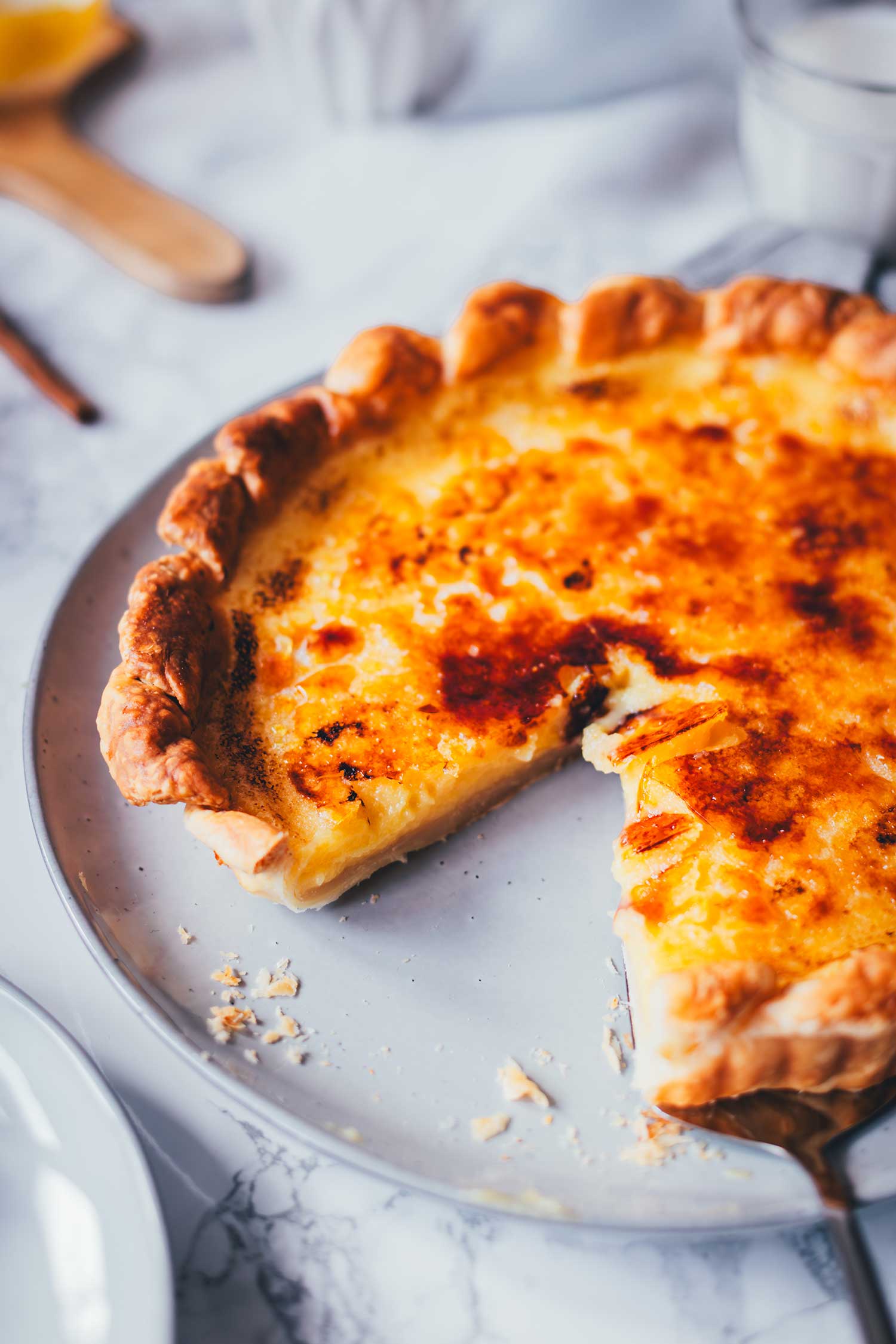 Seitliche Nahaufnahme von einer gerade angeschnittenen Pasteis de Nata Tarte. Man sieht die goldgelbe Füllung die karamellisierte Zuckerschicht.