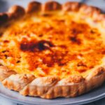 Detaillierte Nahaufnahme von einer frisch gebackenen Pasteis de Nata Tarte – portugiesische Törtchen als große runde Tarte gebacken. Man sieht die goldene Füllung und die karamellisierte Zuckerschicht oben drauf.