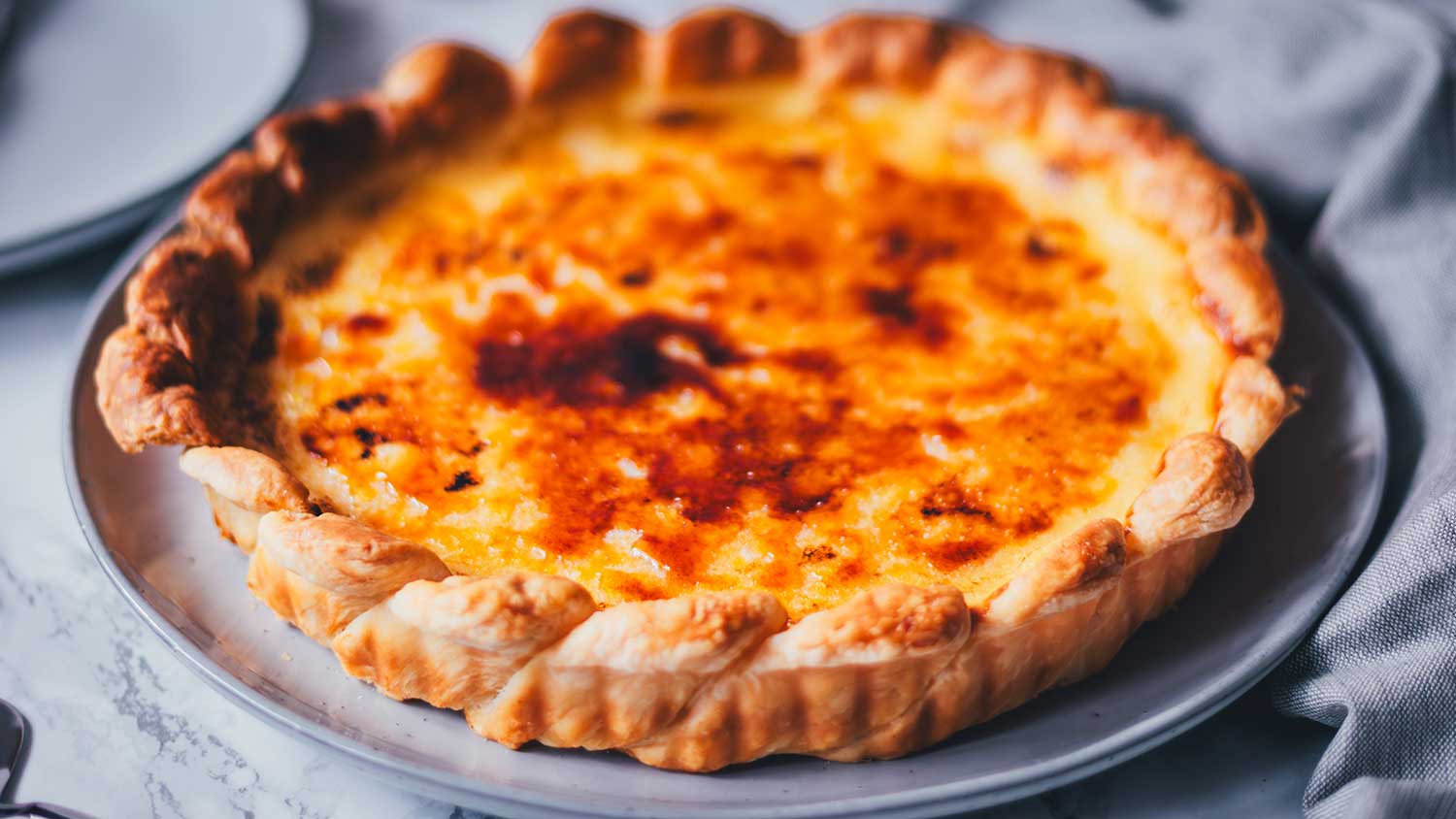 Detaillierte Nahaufnahme von einer frisch gebackenen Pasteis de Nata Tarte – portugiesische Törtchen als große runde Tarte gebacken. Man sieht die goldene Füllung und die karamellisierte Zuckerschicht oben drauf.