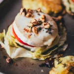 Nahaufnahme eines vegetarischen Spitzkohl-Schnitzels mit cremigem Ziegenkäse, Apfelscheibe und gerösteten Walnüssen.