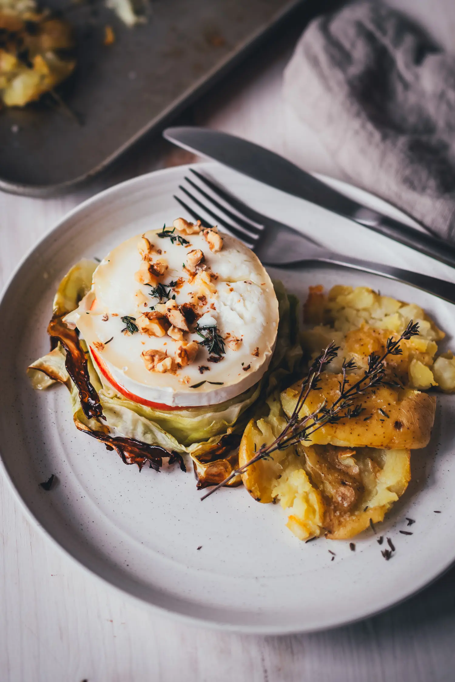 Vegetarisches Spitzkohl-Schnitzel mit Ziegenkäse und Apfel, angerichtet mit Smashed Potatoes und Thymian auf einem hellen Teller.