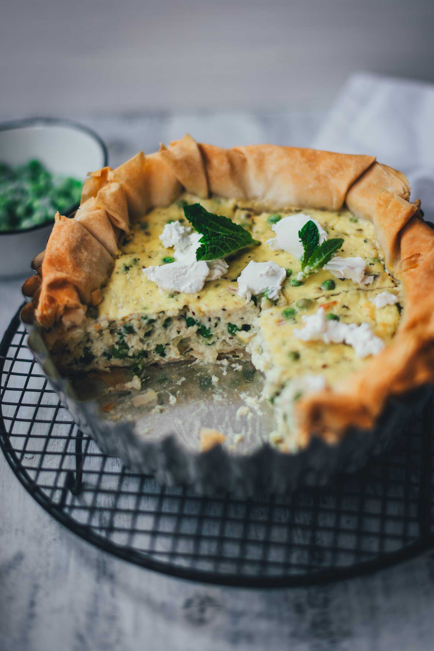 Detailaufnahme des Anschnitts der Erbsen-Ricotta-Quiche mit hoch aufgehender Erbsenfüllung, knusprigem Filoteig-Rand und Tupfen Ziegenfrischkäse.