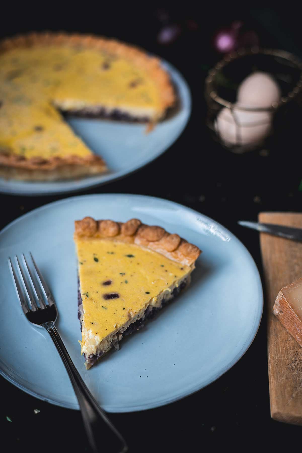 Zwiebelquiche bei 45 Grad fotografiert, Stück auf Teller im Vordergrund, im Hintergrund die angeschnittene Quiche | moeyskitchen.com