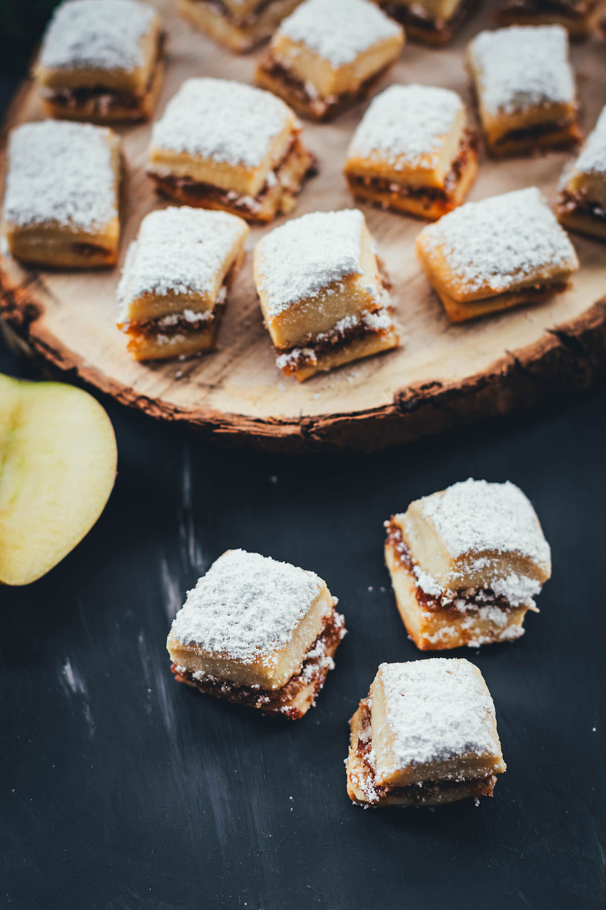 Bratapfel-Stollen-Konfekt in kleinen würfelförmigen Stücken, bestäubt mit Puderzucker, auf Holzbrett angerichtet.