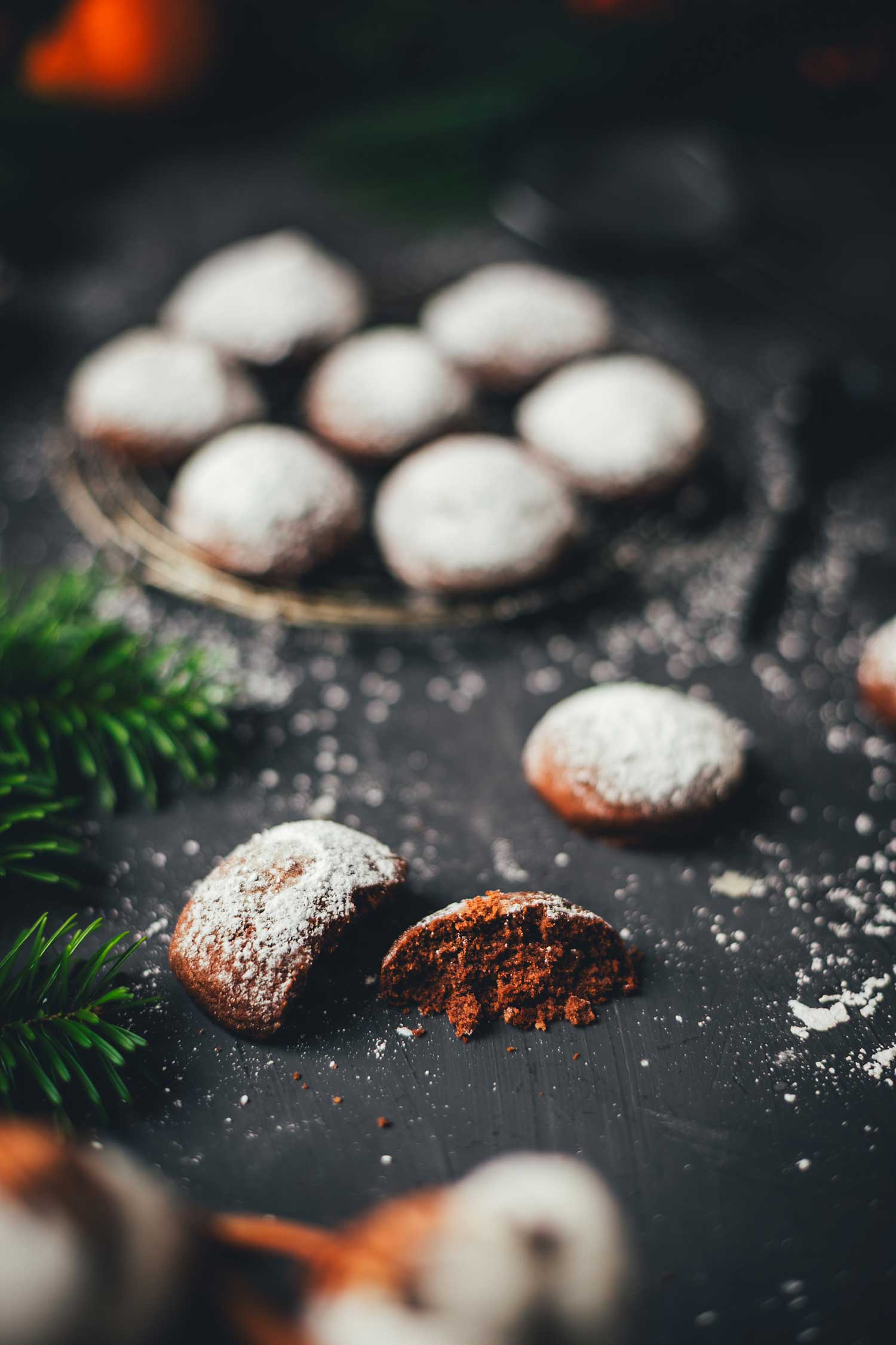 Angeschnittene Espresso-Walnuss-Kekse mit schokoladigem Inneren, bestäubt mit Puderzucker, weihnachtliche Stimmung im Hintergrund.